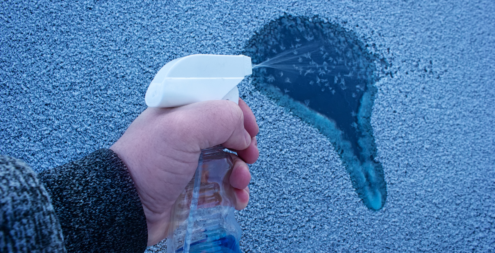 Hand spraying liquid on icy and snowy car window