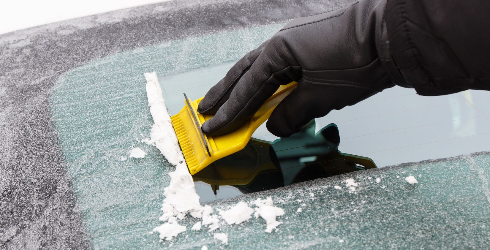 A person de-icing her windshield with a yellow scrapper