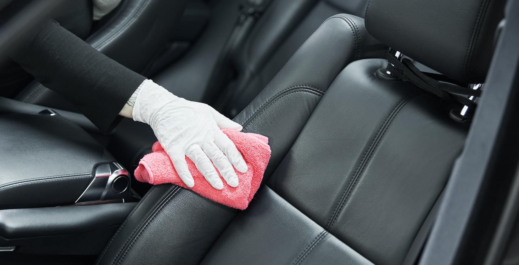 Hand with a plastic glove washing a leather car seat.
